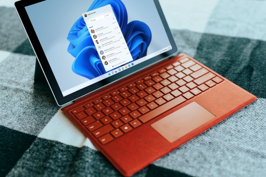 Red Surface laptop on a checkered bed by a window