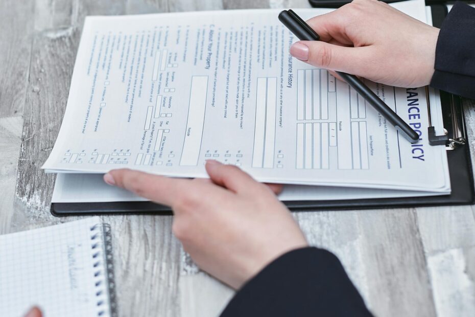 Free Close-up of hands analyzing insurance policy paperwork with pen on table. Stock Photo